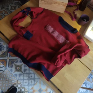 Sur une table en bois, on voit un pull rouge et bleu marine
