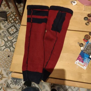 Sur une table en bois, on voit deux manches rouges et bleues marines. À côté sont éparpillés des boutons.