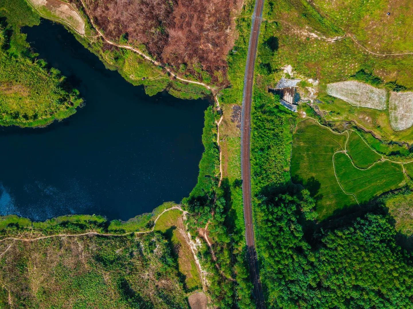Vue du ciel sur une route avec un lac , des chemins, un bois, des sols en friche et d'autres cultivés, des carrières de pierre paraissent en gris.