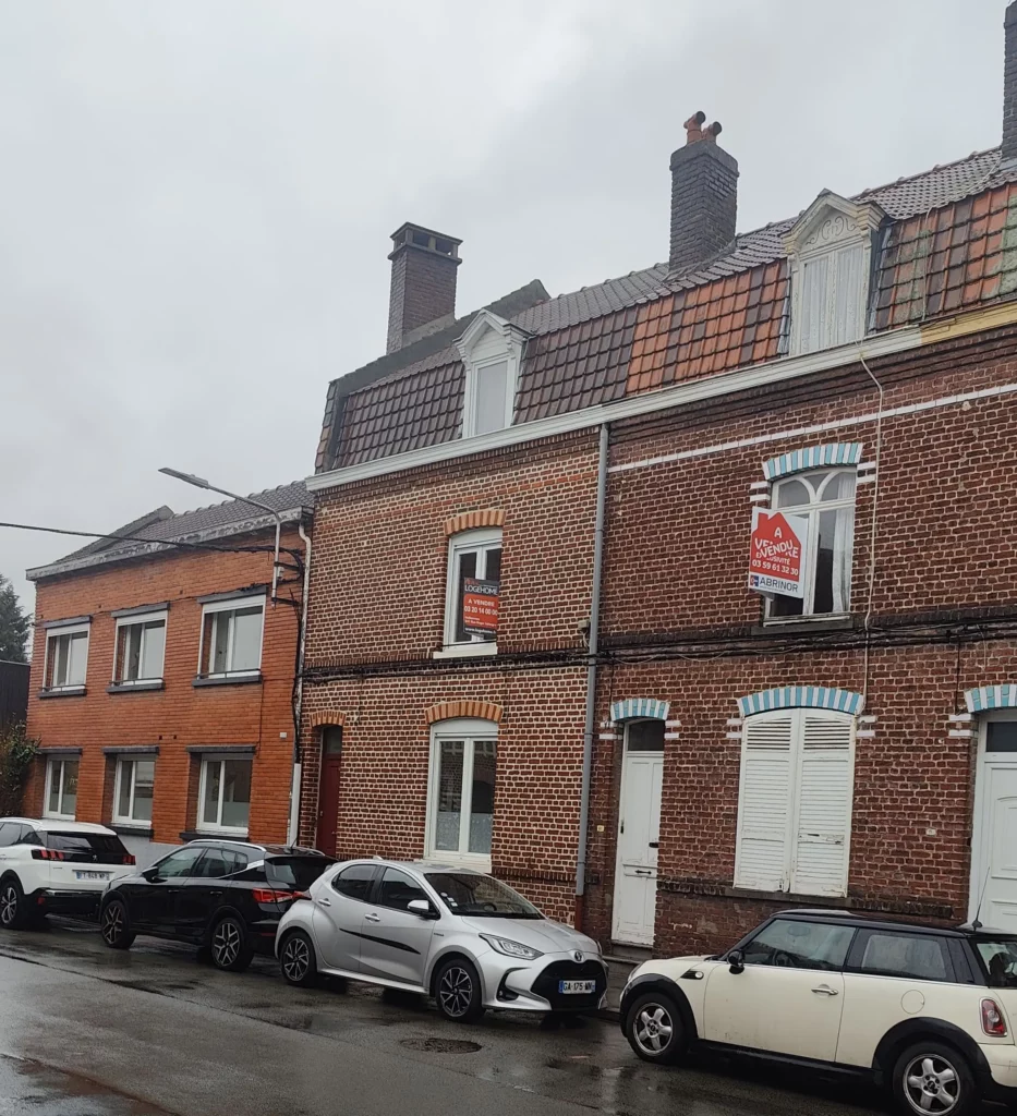 On voit deux maisons de villes mitoyennes sur lesquels des panneaux de mise en vente sont affichés.