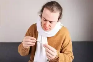 Homme avec écharpe et nez rougis qui lit un thermomètre.