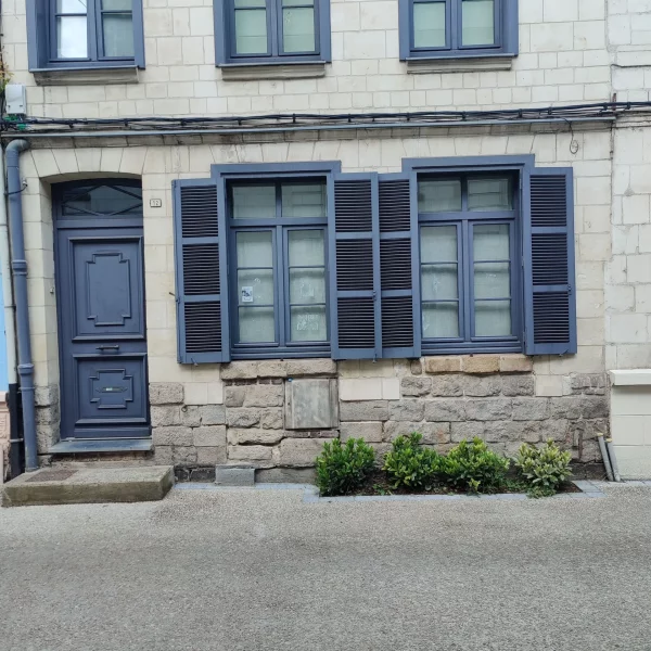 Où l'on voit une maison à menuiseries bleues sur pierres blanches avec un soubassement en grès. On voit des plantations en pied de façade, le rez-de-chaussée et le 1ᵉʳ étage.