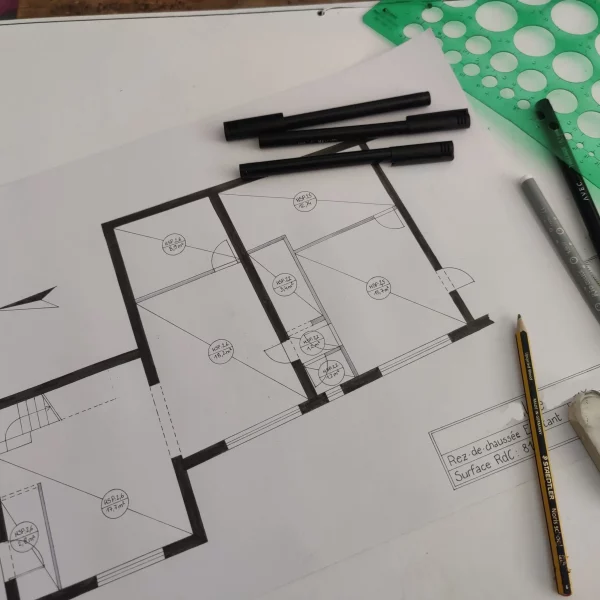 On voit un plan de maison sur lequel traînent des feutres noirs, un crayon de bois et une règle avec différents disques.